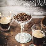 Gorgeous coffee glasses filled with hot coffee and cocktail glass filled with coffee beans standing on dark ground, surrounded by coffee beans.