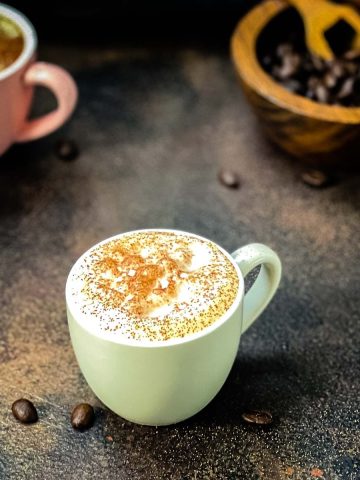 Two cups of coffee on dark brown surface. Milk foam dusted with cocoa.