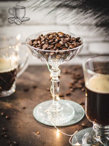 Gorgeous coffee glasses filled with hot coffee and cocktail glass filled with coffee beans standing on dark ground, surrounded by coffee beans.