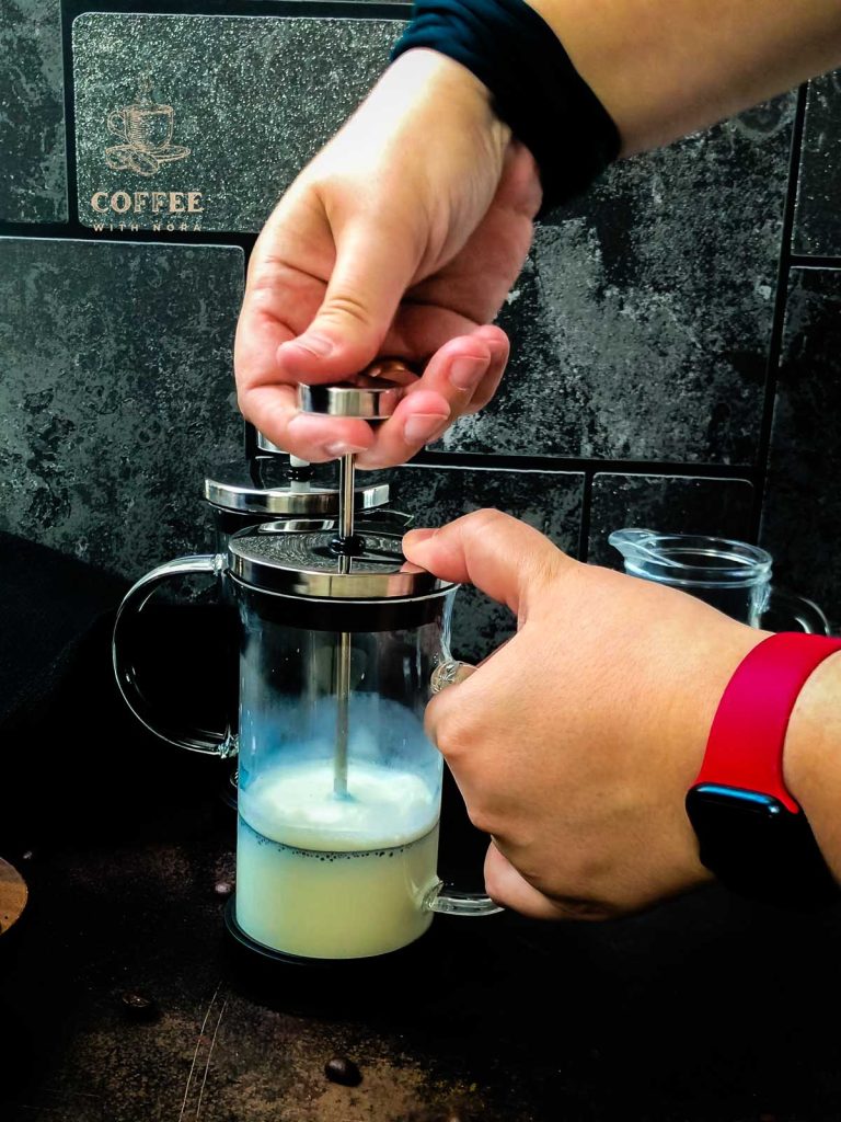 Frothing milk in a French press by moving the plunger quickly up and down below the milks surface.