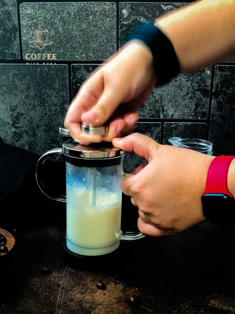 Frothing milk in a French press by moving the plunger quickly up and down below the milks surface.