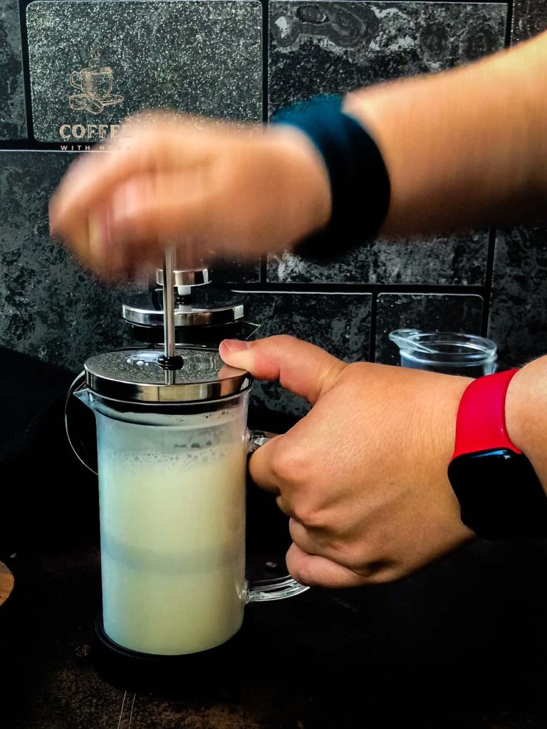 Frothing milk in a French press by moving the plunger quickly up and down below the milks surface.