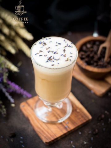 Gorgeous glass with honey lavender latte, sprinkled with dried lavender placed on wooden coaster.