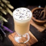 Gorgeous glass with honey lavender latte, sprinkled with dried lavender placed on wooden coaster.