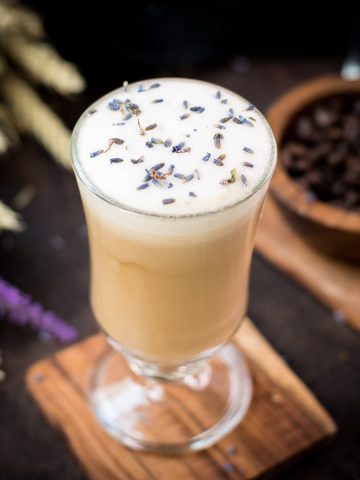 Gorgeous glass with honey lavender latte, sprinkled with dried lavender placed on wooden coaster.