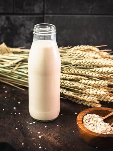 Milk bottle with oat milk on dark background.