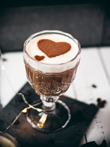 Gorgeous glass filled with coffee con leche on dark slate plate.