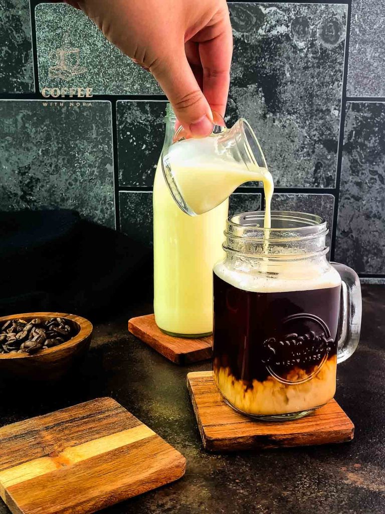 Homemade coffee creamer is poured into a mason jar filled with coffee.