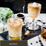 Gorgeous glass filled with iced honey latte placed on dark slate plate.