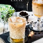 Gorgeous glass filled with iced honey latte placed on dark slate plate.