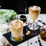 Gorgeous glasses filled with iced honey latte placed on dark slate plate.