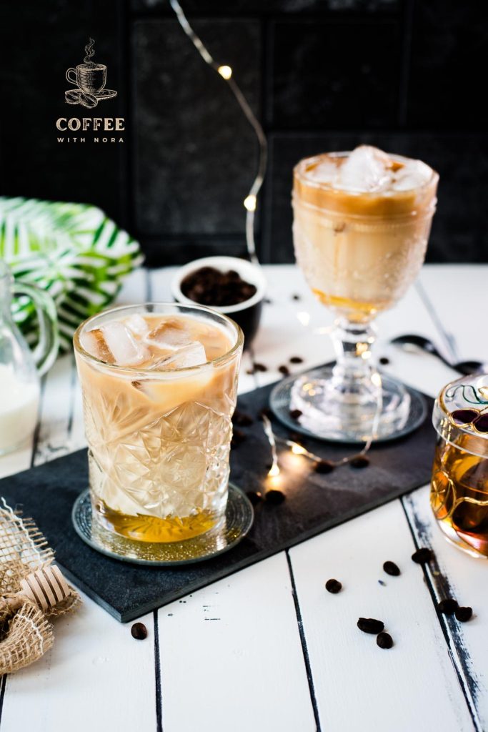 Gorgeous glasses filled with iced honey latte placed on dark slate plate.