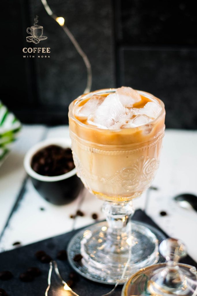 Gorgeous glass filled with iced honey latte placed on dark slate plate.