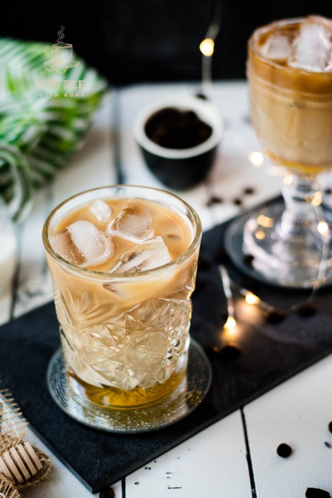 Gorgeous glass filled with iced honey latte placed on dark slate plate.