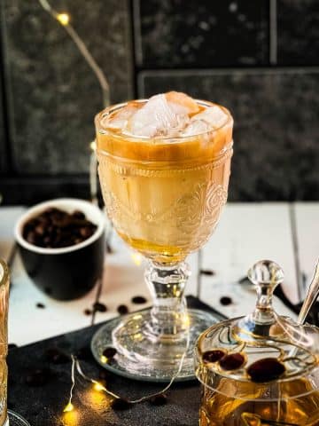 Gorgeous glasses filled with iced honey latte placed on dark slate plate.