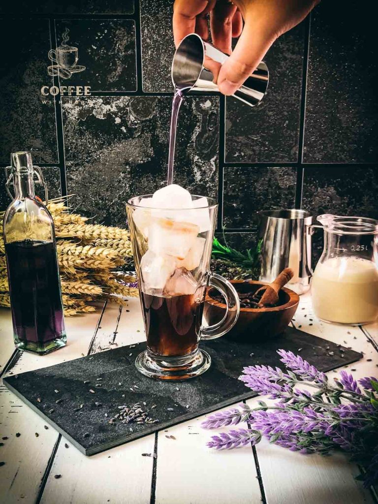 Beautiful glass filled with ice cubes and coffee, drizzled with lavender syrup.