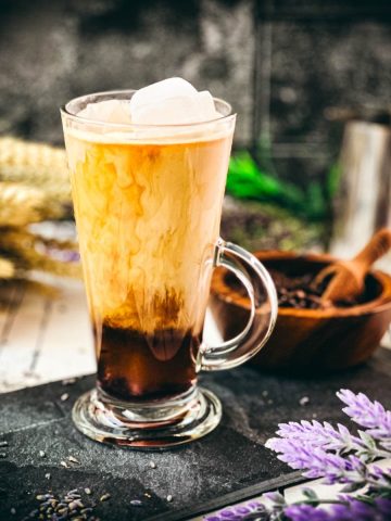 Gorgeous glass filled with iced lavender latte on dark slate plate.