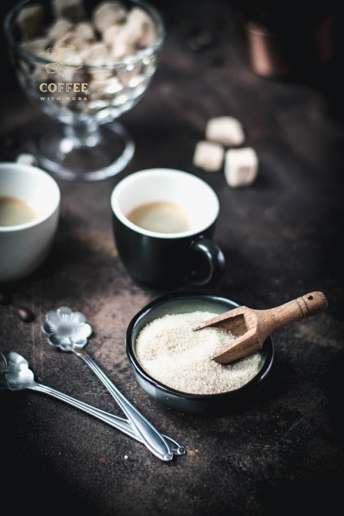 Brown sugar in dark green bowl next to black cup filled with black coffee.