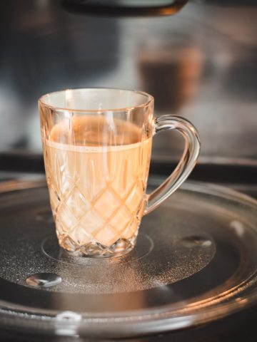 Glass mug filled with coffee and milk placed in microwave.