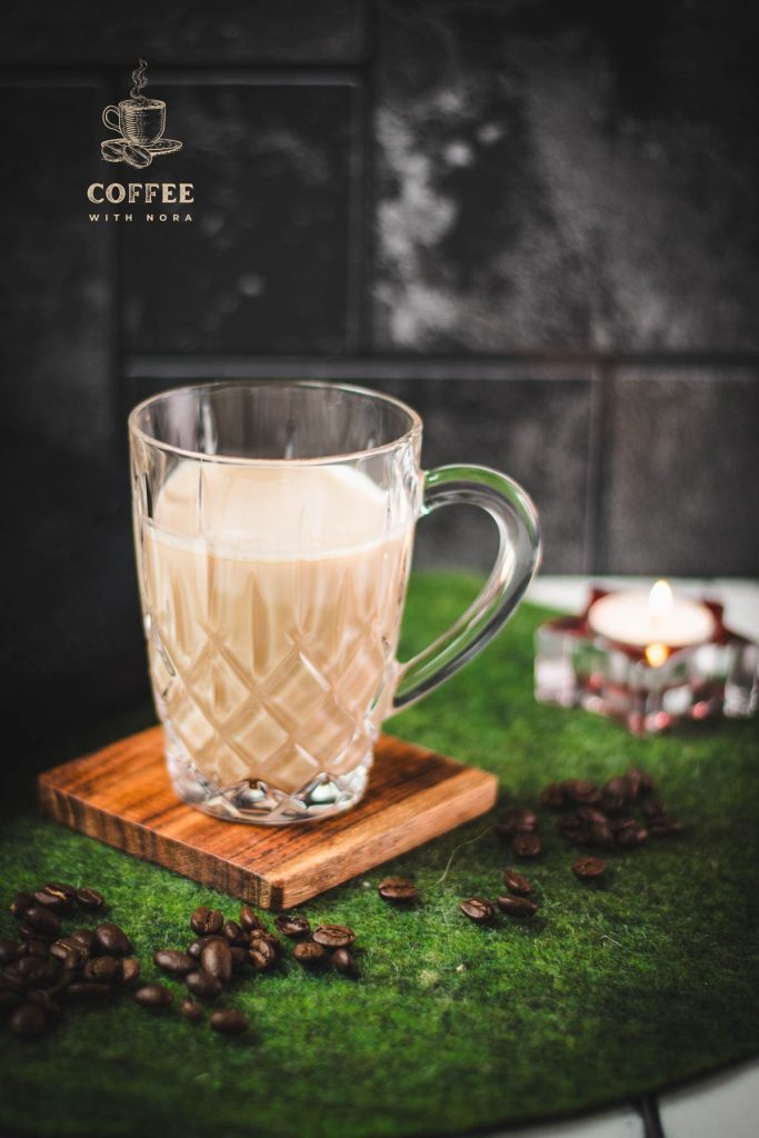 Glass mug filled with coffee and milk, placed on wooden coaster.