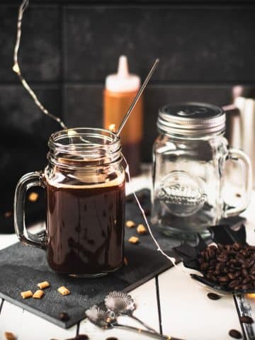 Mason jar filled with delicious coffee caramel. Placed on black slate, surrounded by coffee beans and caramel pieces.