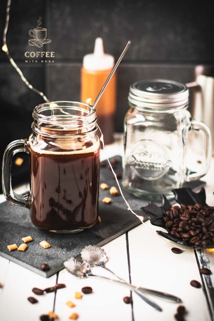 Mason jar filled with delicious coffee caramel. Placed on black slate, surrounded by coffee beans and caramel pieces.