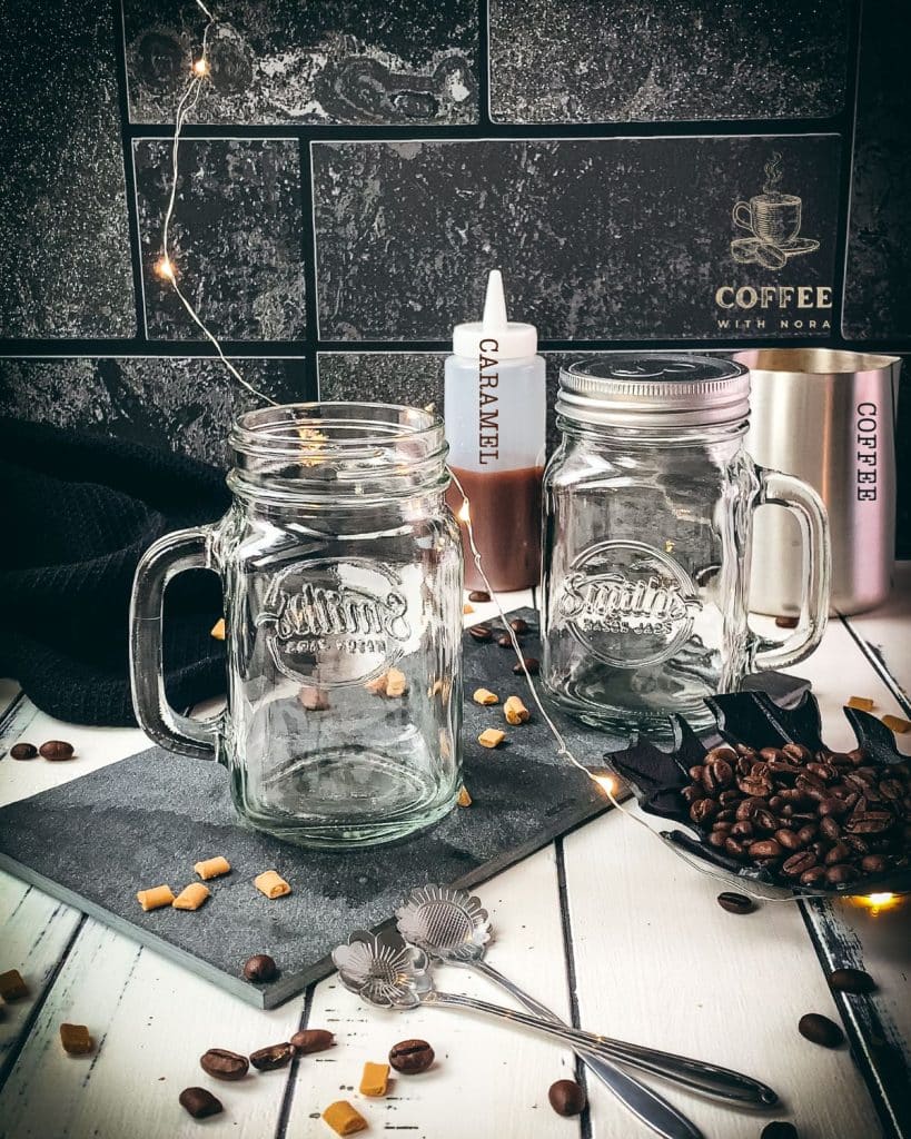 Two mason jars placed on black slate, surrounded by coffee beans and caramel pieces.