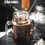 Mason jar filled with delicious coffee caramel. Placed on black slate, surrounded by coffee beans and caramel pieces.