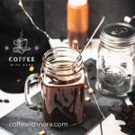 Mason jar filled with delicious coffee caramel. Placed on black slate, surrounded by coffee beans and caramel pieces.