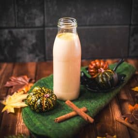 Gorgeous homemade pumpkin spice creamer in a bottle, placed on green felt next to small pumpkins.