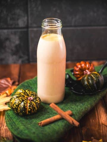 Gorgeous homemade pumpkin spice creamer in a bottle, placed on green felt next to small pumpkins.