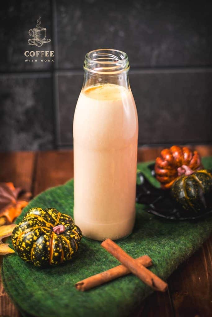 Gorgeous homemade pumpkin spice creamer in a bottle, placed on green felt next to small pumpkins.