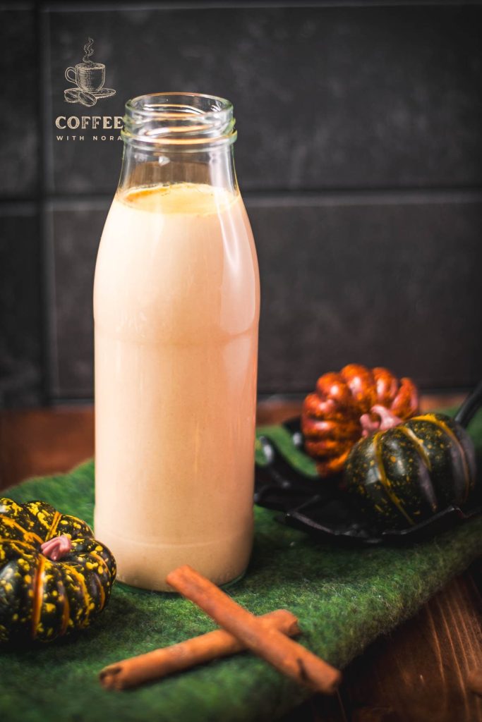 Gorgeous homemade pumpkin spice creamer in a bottle, placed on green felt next to small pumpkins.