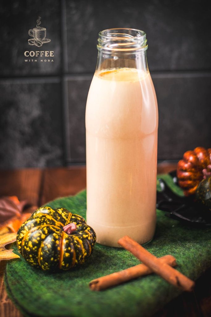 Gorgeous homemade pumpkin spice creamer in a bottle, placed on green felt next to small pumpkins.