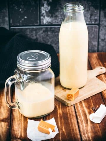 A bottle and a mason jar, filled with scrumptious homemade salted caramel coffee creamer. Placed on wooden board.