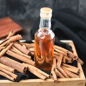 Preserving bottle filled with delectable brown sugar cinnamon syrup placed in wooden basket filled with cinnamon sticks.