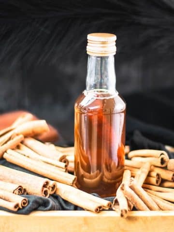 Preserving bottle filled with delectable brown sugar cinnamon syrup placed in wooden basket filled with cinnamon sticks.