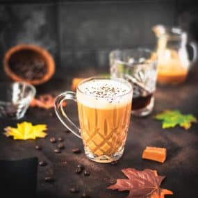 Gorgeous, amber colored caramel coffee with homemade caramel milk filled in glass mug and placed on dark ground.