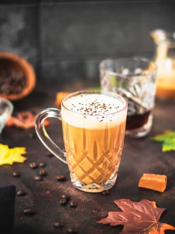 Gorgeous, amber colored caramel coffee with homemade caramel milk filled in glass mug and placed on dark ground.