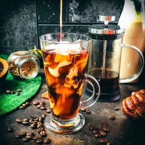 Delicious Pumpkin cream cold brew in gorgeous glass next to French press coffee maker.