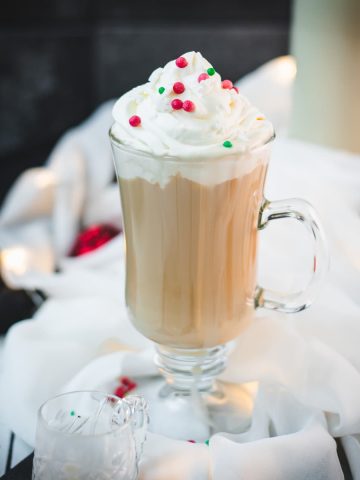 Festive Christmas coffee with homemade Christmas creamer. Topped with whipped cream and sprinkled with Christmassy placed on white ground.