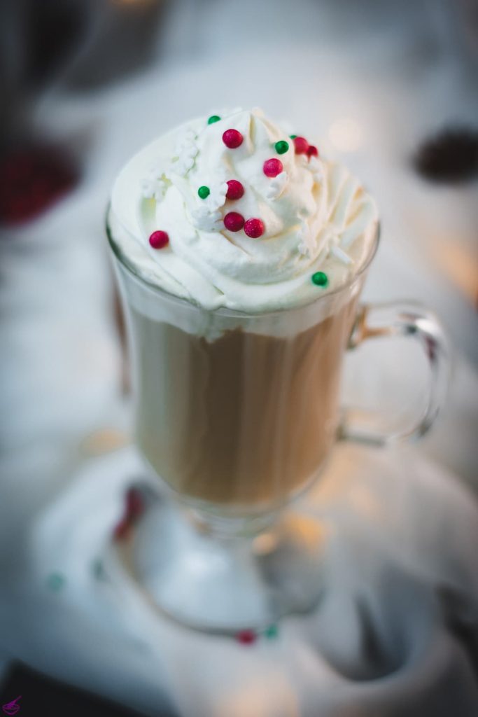 Festive Christmas coffee with homemade Christmas creamer. Topped with whipped cream and sprinkled with Christmassy placed on white ground.