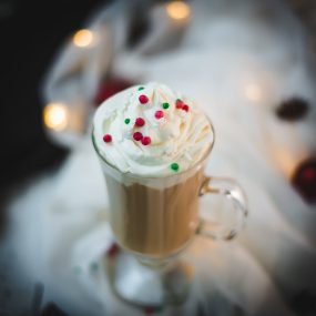 Festive Christmas coffee with homemade Christmas creamer. Topped with whipped cream and sprinkled with Christmassy placed on white ground.