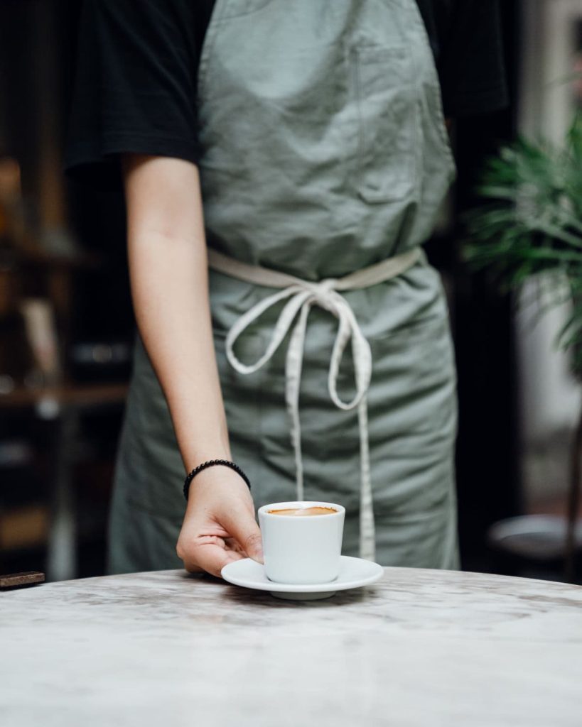 Barista who places a cappuccino on the table.