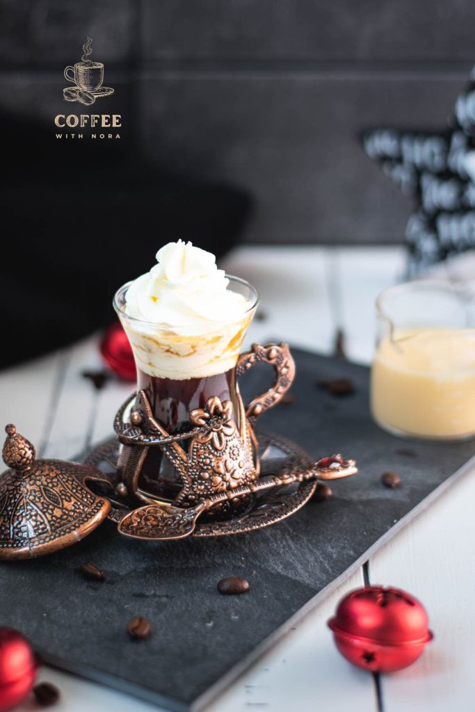 Gorgeous mediaeval coffee glass filled with black coffee, topped with eggnog flavored whipped cream. Placed on black slate plate next to a glass of eggnog.