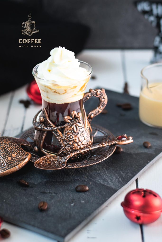 Gorgeous mediaeval coffee glass filled with black coffee, topped with eggnog flavored whipped cream. Placed on black slate plate next to a glass of eggnog.