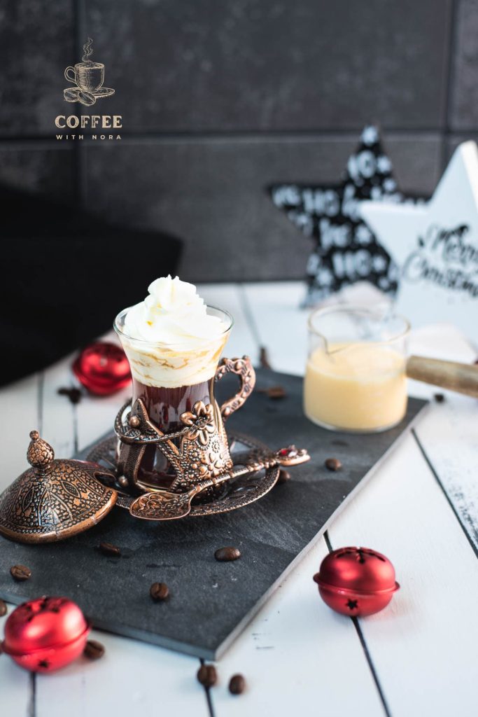 Gorgeous mediaeval coffee glass filled with black coffee, topped with eggnog flavored whipped cream. Placed on black slate plate next to a glass of eggnog.