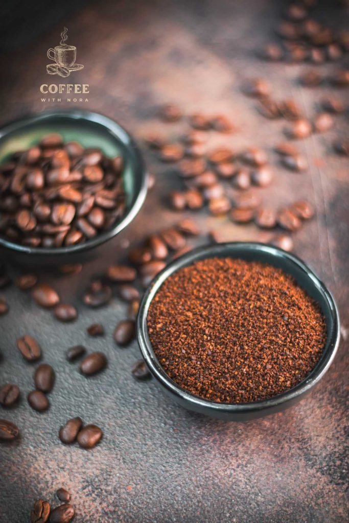 Two bowls each filled with coffee beans and grated coffee on rust brown background surrounded by coffee beans.