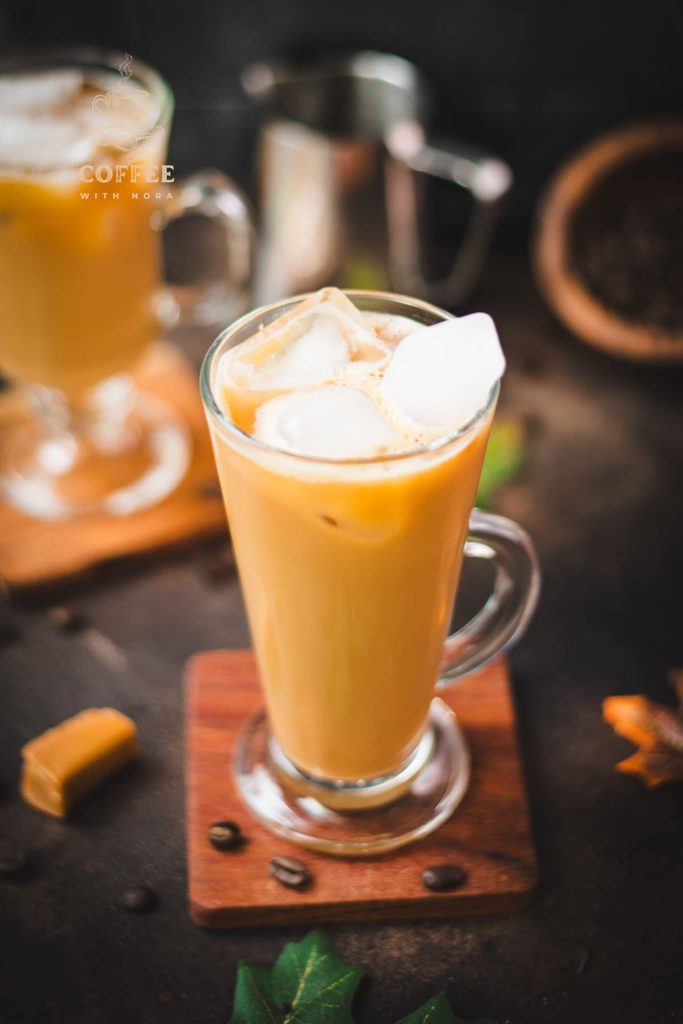 Tall, narrow coffee glass filled with iced caramel latte, with homemade caramel milk. Placed on wooden coaster.