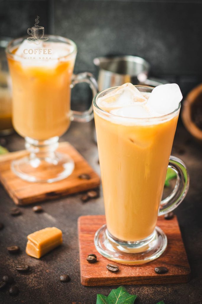 Tall, narrow coffee glass filled with iced caramel latte, with homemade caramel milk. Placed on wooden coaster.